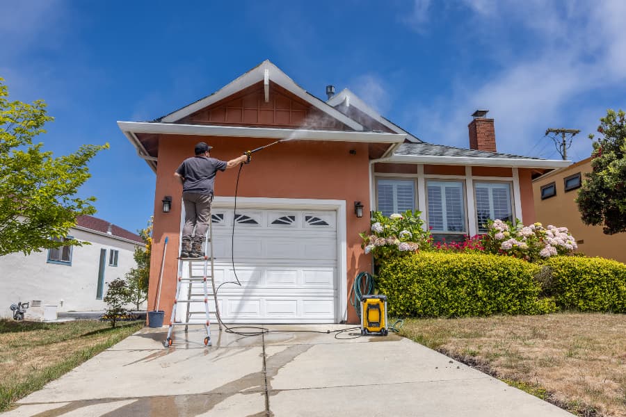Worker On Ladder Power Washing Home Exterior Worker On Ladder Power Washing Home Exterior