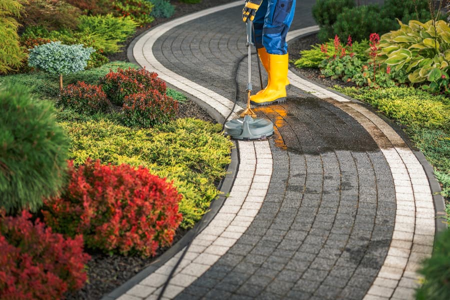 Person Power Washing Residential Garden Pathway Using Concrete Attachment Person Power Washing Residential Garden Pathway Using Concrete Attachment